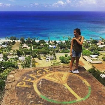 AIFS Au Pair in Hawaii steht auf einem auf Stein gemalten Peace Sign