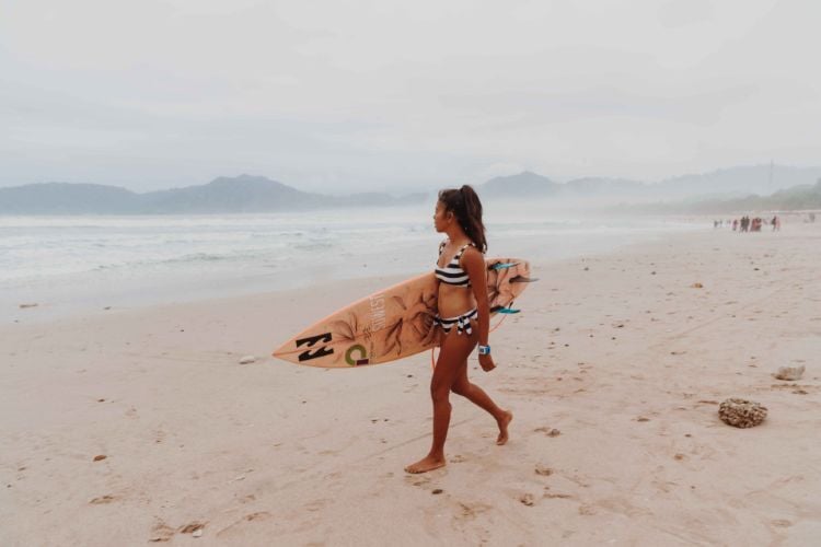 Person mit Surfboard am Strand beim Surfcamp in Canggu, Bali mit AIFS