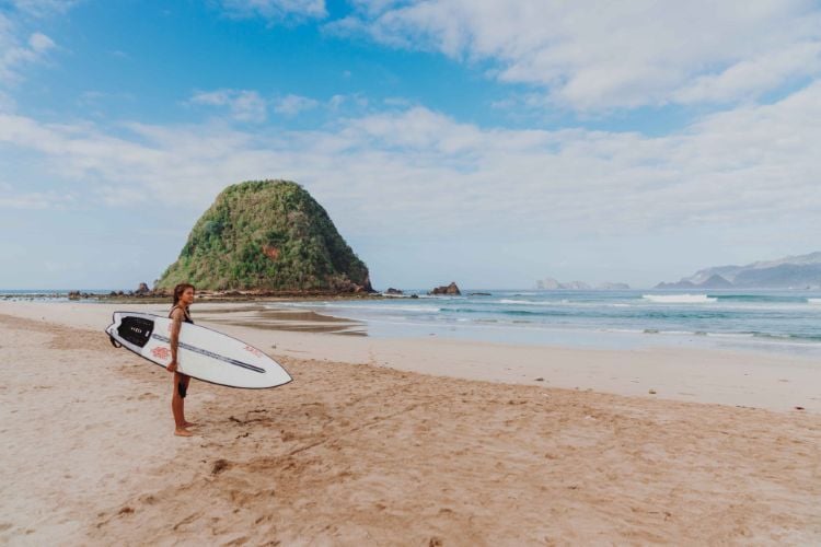 Eine Teilnehmerin mit Surfboard am Strand beim Surfcamp in Red Island, Bali mit AIFS
