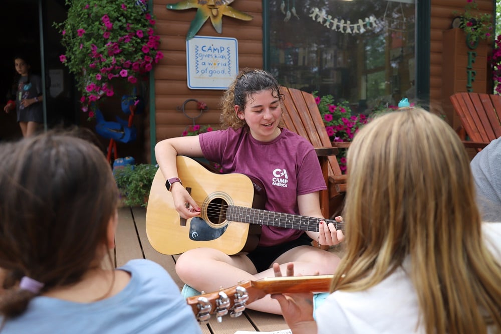 AIFS Teamer bringt den Kindern Gitarrespielen im Camp America bei